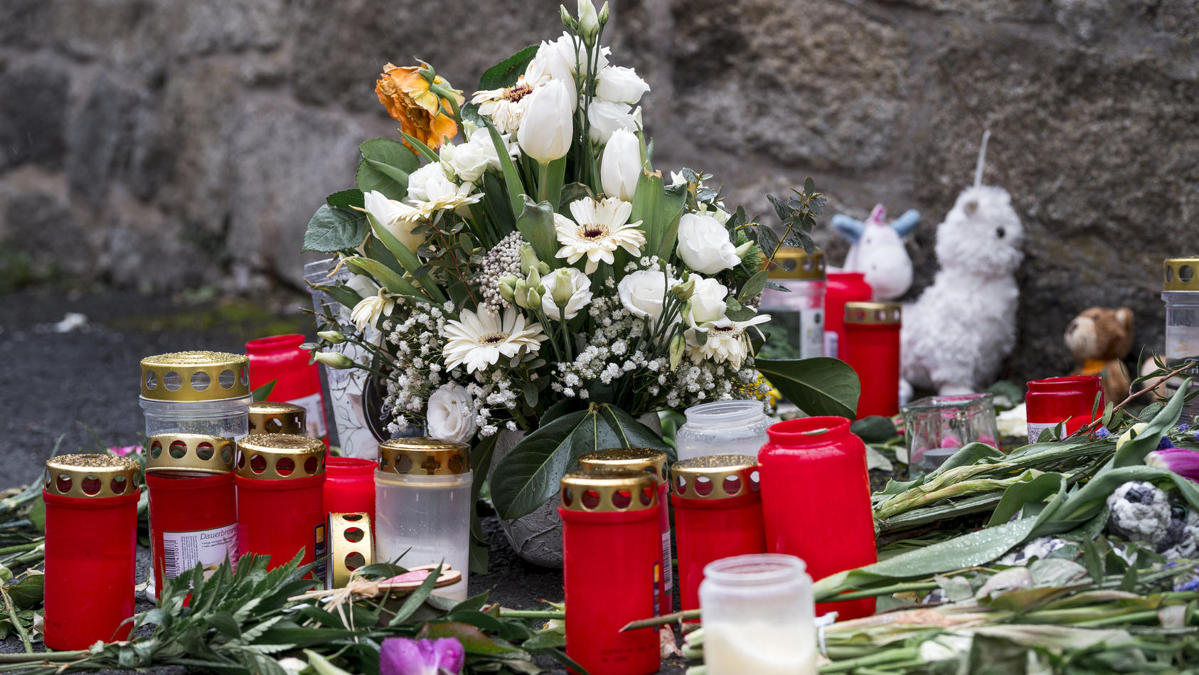12.04.2023, Bayern, Wunsiedel: An der Straßenecke zur Zufahrtsstraße zum Kinder- und Jugendhilfezentrum, in dem eine Zehnjährige tot aufgefunden wurde, liegen Blumen, Kuscheltiere und Grablichter auf dem Gehweg. Foto: Daniel Vogl/dpa +++ dpa-Bildfunk