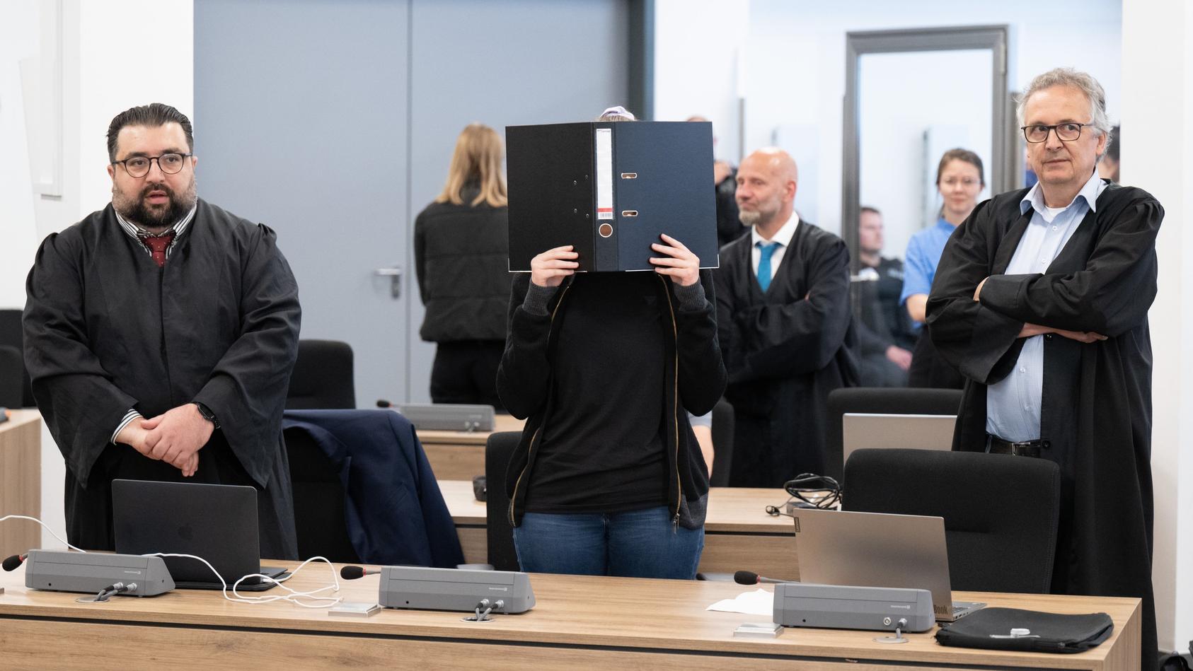 Die Angeklagte Lina E. (mitte) steht bei der Fortsetzung des Prozesses im Oberlandesgericht (OLG) Dresden im Verhandlungssaal und hält einen Aktenordner vor ihr Gesicht.