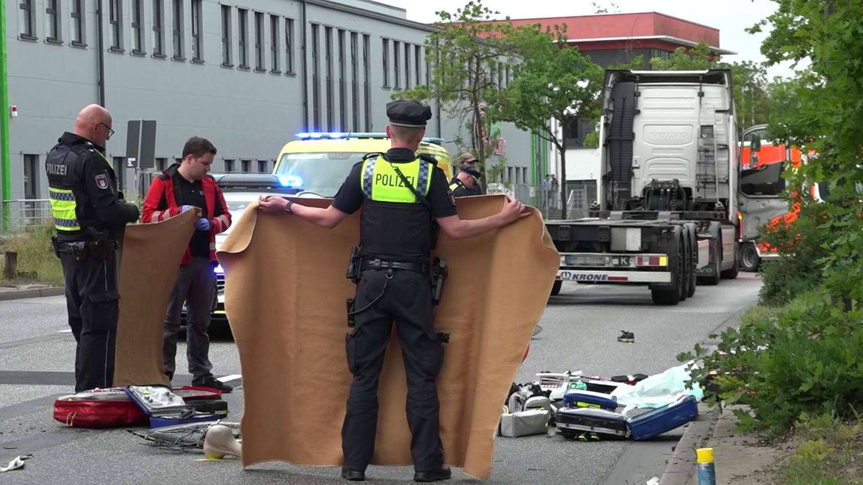 Einsatzkräfte schirmen das Unfallopfer ab. Im Hintergrund steht der LKW, der den Radfahrer überrollt hat.