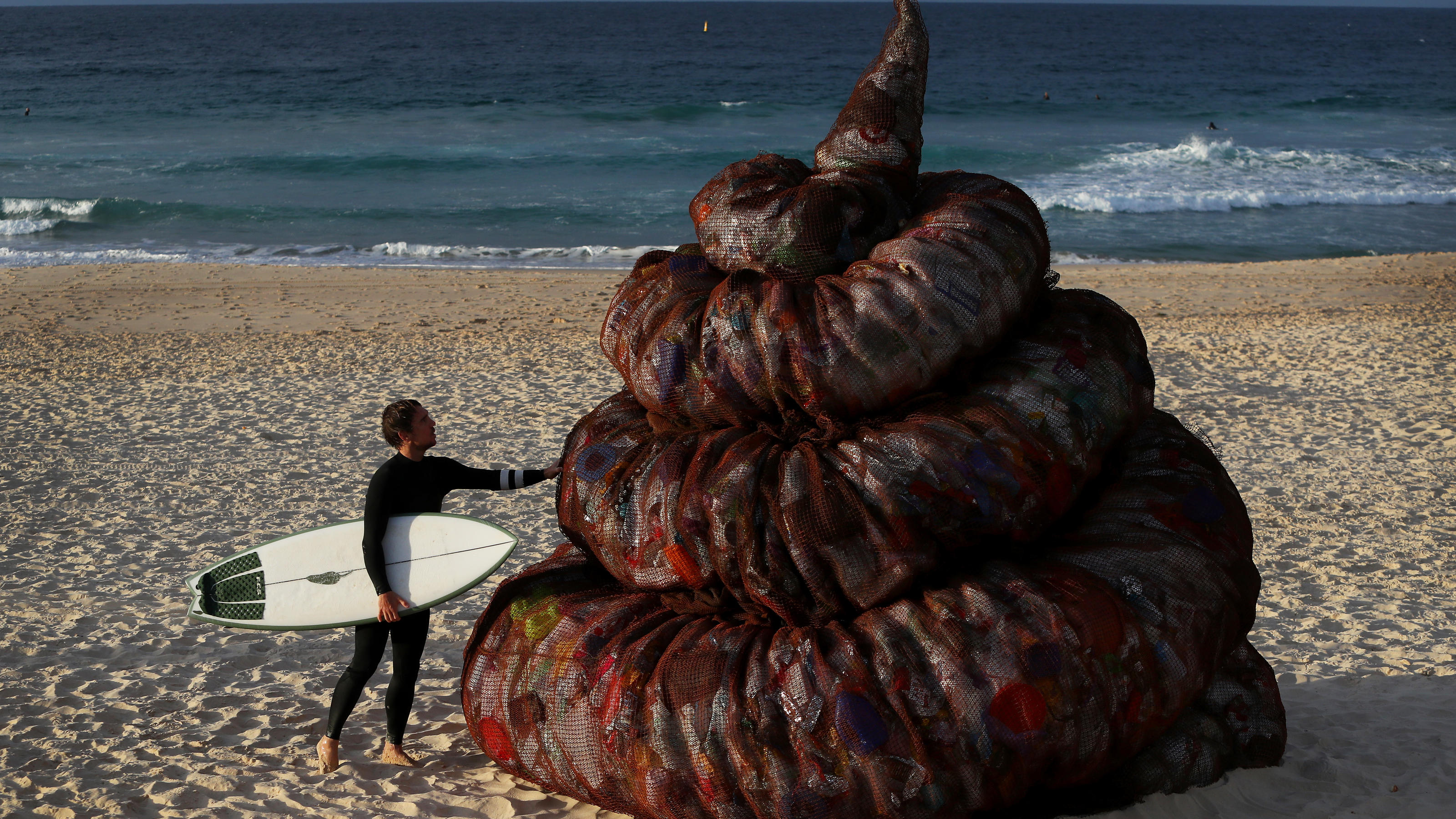 SYDNEY, AUSTRALIA - JUNE 05: A surfer interacts with a sculpture titled 'Plastic pile of sh!t, 2023' presented by Better Packaging Co. at Bondi Beach on June 05, 2023 in Sydney, Australia. The four-metre-high sculpture is made out of recycled plastic