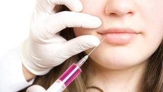 Doctor making injection in lips of young woman 