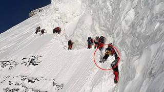 Drohnenaufnahmen zeigen dutzende Bergsteiger auf dem Weg zum Gipfel des K2. Ein Mann liegt flach und fixiert an einer Felswand.