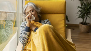 Mature woman with tissue blowing nose by window at home model released, Symbolfoto property released, JCCMF10163