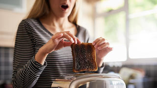 Frau hält einen verbrannten Toast in der Hand.