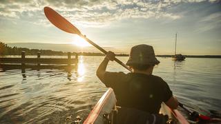  Eine Frau fährt mit ihrem Kajak auf dem Starnberger See dem Sonnenuntergang entgegenan, Starnberg, Bayern, Deutschland. Eine Frau paddelt auf einer Kajaktour auf dem Starnberger See
