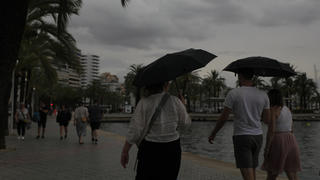 02.09.2023, Spanien, Palma: Mit Schirmen sind Spaziergänger an der Strandpromenade unterwegs. Auf Mallorca wurde wegen möglicher Unwetter die gelbe Alarmstufe ausgerufen. Foto: Clara Margais/dpa +++ dpa-Bildfunk +++