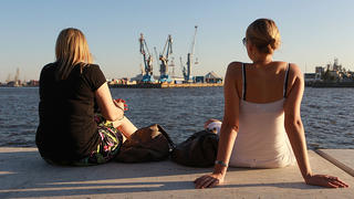 ARCHIV - Bei sommerlicher Wärme genießen zwei junge Frauen am 01.10.2011 im Hafen von Hamburg die Sonne. Die Euro-Krise nagt offenbar noch nicht am Glück der Deutschen: In einer aktuellen Glücksstudie geben sie ihrer Lebenszufriedenheit genau wie im Vorjahr exakt sieben von zehn Punkten und damit den höchsten Wert seit 2011. Die glücklichsten Deutschen leben demnach auch in diesem Jahr in Hamburg. Foto Ulrich Perrey/lno  +++(c) dpa - Bildfunk+++