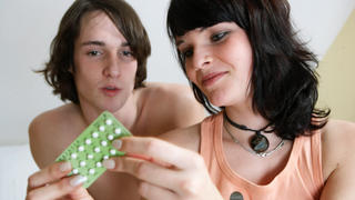 Eine junge Frau sitzt mit einer Packung der "Pille" zur Schwangerschaftsverhütung auf einem Bett und ihr Freund schaut interessiert, aufgenommen am 02.12.2006 in Berlin (Symbolbild zum Thema Beziehung, Sexualität, Erotik, Liebe, Schlafzimmer, Verantwortung,Verhütung, Schwangerschaftsverhütung,Pille). Foto: Jörg Lange  - Model relase vorhanden - +++(c) dpa - Report+++