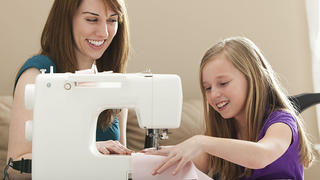 Junge Frau arbeitet an der Nähmaschine, Kind hilft Keine Weitergabe an Drittverwerter.