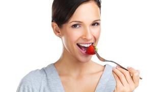 nette Brünette isst eine Schale Erdbeeren, lächelt in die Kamera