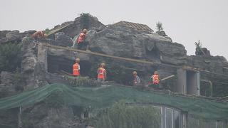Workers demolish parts of a privately built villa, surrounded by imitation rocks, on the rooftop of a 26-storey residential building, on a hazy day in Beijing August 16, 2013. A Chinese property owner has started dismantling an 800-square-metre villa built illegally, complete with a garden, on top of a Beijing apartment block after complaints from his neighbours and a government warning to tear it down. On Monday, authorities demanded that Zhang Biqing, the villa's builder, demolish it within 15 days. REUTERS/China Daily (CHINA - Tags: SOCIETY BUSINESS CONSTRUCTION REAL ESTATE) CHINA OUT. NO COMMERCIAL OR EDITORIAL SALES IN CHINA
