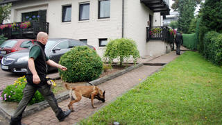 Ein Hundeführer geht am 03.09.2013 in Eslohe (Nordrhein-Westfalen) auf einen Hauseingang zu. Die Polizei hat zwei Babyleichen in dem Haus eines Ehepaares im sauerländischen Eslohe entdeckt. Bei einem Baby, das vermutlich in der vergangenen Woche zur Welt gekommen war, ergab die Obduktion keine Spuren eines gewaltsamen Todes. Das teilte die Staatsanwaltschaft mit. Foto: Jörg Taron/dpa +++(c) dpa - Bildfunk+++