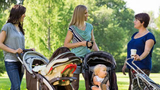Happy mothers with baby strollers talking in park