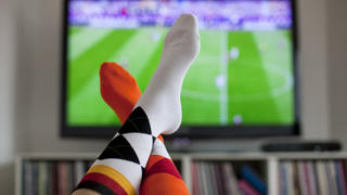 ARCHIV - ILLUSTRATION - Überschlagene Beine vor einem Fernsehgerät, auf dem ein Fußballspiel übertragen wird, aufgenommen am 13.06.2012 in Köln. Foto: Rolf Vennenbernd (zu dpa Fernsehen bestimmt die Freizeit vom 29.08.2013) +++(c) dpa - Bildfunk+++