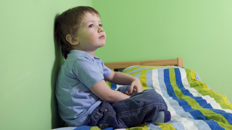 Umzug mit Kind: Junge sitzt nachdenklich auf Bett