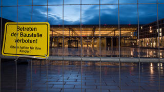 ARCHIV - Blick durch einen Bauzaun auf das am Abend beleuchtete Terminal des neuen Flughafens Berlin Brandenburg Willy Brandt (BER) in Schönefeld (Brandenburg) am 10.01.2013. Beim Bau des neuen Hauptstadtflughafens sind Nachforderungen von Baufirmen in Höhe von mehr als 1,4 Milliarden Euro eingereicht worden. Foto: Patrick Pleul/dpa (zu dpa "Hauptstadtflughafen: Nachforderungen von mehr als 1 Milliarde Euro" vom 07.06.2014) +++(c) dpa - Bildfunk+++