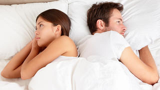 Upset young couple having marital problems or a disagreement lying side by side in bed facing in opposite directions ignoring one another. Interracial couple, Asian woman, Caucasian man.