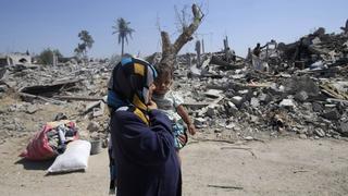A Palestinian woman holds her daughter as they walk past the ruins of destroyed houses in Khuzaa town, which witnesses said was heavily hit by Israeli shelling and air strikes during Israeli offensive, in the east of Khan Younis in the southern Gaza Strip August 6, 2014. With its spacious villas and palm-lined streets, the town of Khuzaa in southern Gaza gave Palestinians a rare place to spend their free time before it was bombed and shelled to rubble last month. Largely free of the local tensions and feuds found in other neighbourhoods, Khuzaa's green spaces were one of just a few destinations for daytrips in the crowded Gaza Strip, where 1.8 million people live in just 360 sq km (140 sq miles). Around 500 metres from the Israeli border, Khuzaa is now only accessible via cratered roads strewn with debris. Nearly all of its homes have been flattened and its nine mosques lie in pieces. Picture taken August 6, 2014. REUTERS/Ibraheem Abu Mustafa (GAZA - Tags: POLITICS CIVIL UNREST)