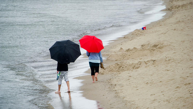 Touristen laufen im Regen am Strand entlang.