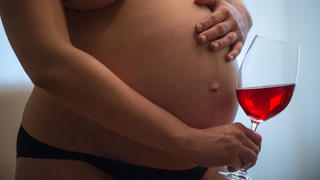 Eine nackte junge schwangere Frau hält ein Glas Wein in der rechten Hand, während die linke auf ihrem Bauch liegt. Foto: Hans Wiedl . Foto: Hans Wiedl  - Model Released
