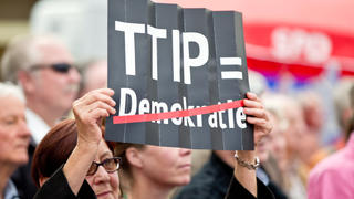 Eine Zuhörerin einer Europawahlkampfveranstaltung der SPD protestiert am 19.05.2014 in Nürnberg (Bayern) mit einem Plakat mit der Aufschrift "Stoppen Sie TTIP" gegen das geplante EU-US-Freihandelsabkommen TTIP. Foto: Daniel Karmann/dpa