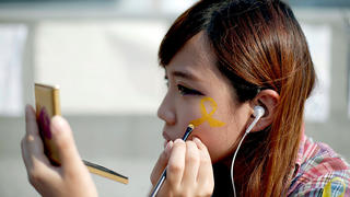 ARCHIV - Eine junge Frau malt am 08.10.2014 in Hongkong eine gelbe Schleife auf ihre Wange, das Symbol der Anhänger der Studentenbewegung. Doch viele der schätzungsweise 10 000 Studenten aus China, die in der ehemaligen britischen Kolonie studieren, haben ambivalente Gefühle gegenüber den Protesten. EPA/MAST IRHAM (zu dpa "Studenten aus China zu Protesten in Hongkong: «Wir denken da anders»" vom 13.10.2014) +++(c) dpa - Bildfunk+++