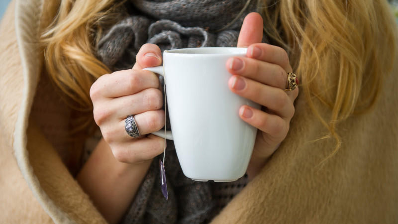 Frau wärmt ihre Hände an Tasse mit heißem Tee