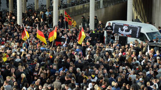 Demonstranten stehen am 26.10.2014 in Köln (Nordrhein-Westfalen) vor einem Fahrzeug mit einem Transparent der als gewaltbereit bekannten Gruppe «Hooligans gegen Salafisten» (HoGeSa). Etwa 1500 Hooligans aus Fangruppen verschiedener Fußballvereine haben sich angekündigt, um gegen Islamisten zu demonstrieren. Foto: Caroline Seidel/dpa +++(c) dpa - Bildfunk+++
