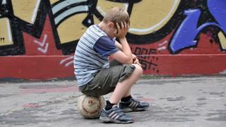 Frustrierter neunjähriger Junge mit Fußball im Grafitti-bunten Hinterhof eines alten Mehrfamilienhauses. August 2009 - model released. Köln, Nordrhein-Westfalen, Deutschland, 11.08.2009