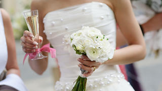 Bride is holding a wedding bouquet and a glass of champagne