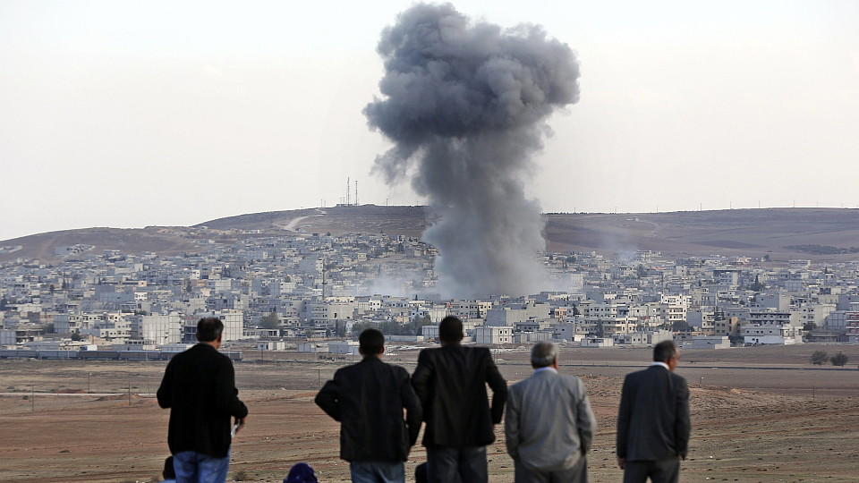 Männer beobachten, wie Rauch in den Himmel über der syrischen Stadt Kobane steigt.