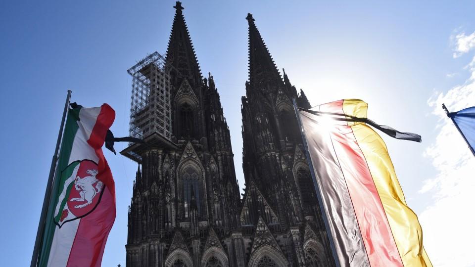Eine NRW Landesfahne und eine Deutschlandfahne mit Trauerflor wehen m 17.04.2015 in Köln (Nordrhein-Westfalen) vor der Trauerfeier für die Opfer des Germanwings-Absturzes vor dem Dom. Bei dem Flugzeugabsturz in den französischen Alpen waren am 24. Mä
