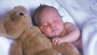 Ein Baby schläft mit seinem großen Teddy im Arm zufrieden ein. Model released.