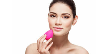 Beautiful young woman applying makeup using beauty blender sponge. Isolated over white background