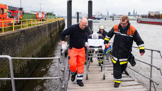 Einsatzkräfte bringen am 27.06.2015 in Hamburg nach einem Bootsunfall auf der Elbe einen verletzten Passagier zum Rettungswagen. Ein Schnellboot ist am Samstag im Stadtteil Kleiner Grasbrook nahe der Elbbrücken gegen einen Ponton gefahren, dabei wurden fünf Insassen verletzt. Foto: Daniel Bockwoldt/dpa +++(c) dpa - Bildfunk+++