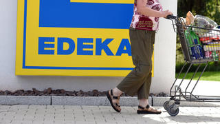 Eine Frau läuft am 26.06.2015 in Schluchsee (Baden-Württemberg) mit ihrem Einkaufswagen an einem Edeka-Logo vorbei. Edeka Südwest hat im Jahr 2014 einen Umsatz von rund sechs Milliarden Euro gemacht. Foto: Patrick Seeger/dpa +++(c) dpa - Bildfunk+++