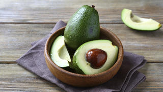 Avocado whole and halves, healthy food on a wooden boards