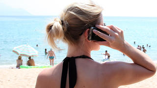 ARCHIV - Ein Frau mit Mobiltelefon steht am 11.07.2012 im griechischen Touristenort Sarti am Strand. Das EU-Parlament stimmt am 27.10.2015 über die weitgehende Abschaffung der Extra-Gebühren für das Telefonieren im EU-Ausland ab. Foto: Friso Gentsch dpa +++(c) dpa - Bildfunk+++