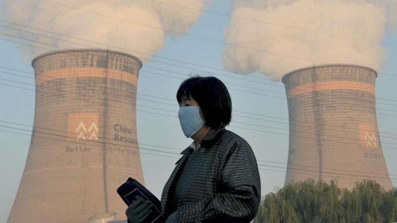Eine Anwohnerin geht am Kühlturm eines Kohle-Heizkraftwerks in Shenyang im Nordosten Chinas vorbei.