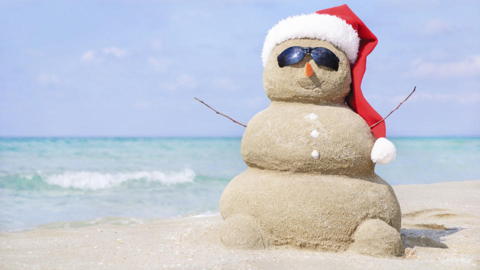 Smiling sandy snowman in red santa hat on the sea beach. Holiday concept can be used for New Year and Christmas Cards