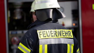 Themenbild - FeuerwehrBild: Feuerwehrmann im Einsatz mit Feuerwehrhelm und Feuerwehranzugvon hintenSymbolbild, Themenbild, Featurebild, Feuerwehr