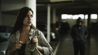 A terrified young woman in an underground parking garage being followed by a sinister man