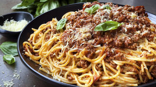 Spaghetti bolognese in black serving platter, with fresh basil and parmesan.