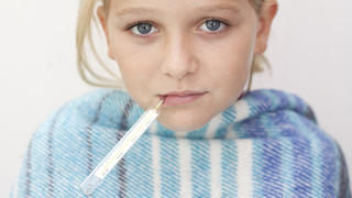 Close up of child with fever thermometer, wrapped in blanket