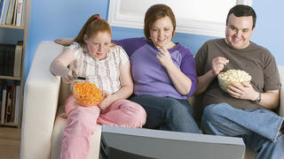Overweight family watching television on sofa