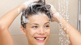 Woman washing hair with shampoo foam in shower smiling happy looking at running warm water. Beautiful mixed race Asian Chinese / Caucasian female model in bathroom.