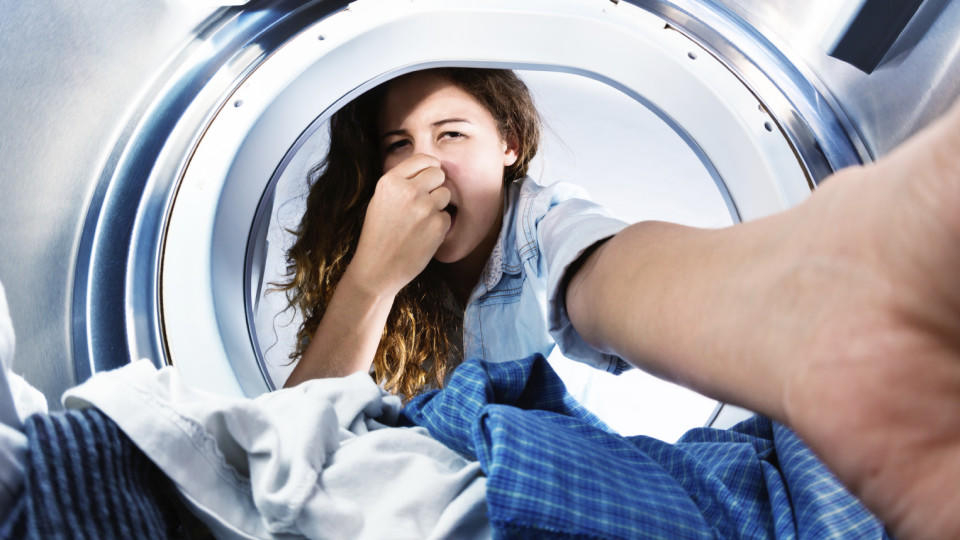 Frau greift in Waschmaschine und hält sich die Nase zu