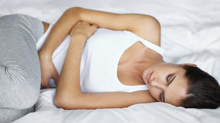 Shot of an attractive young woman lying in bed with cramps