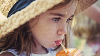 Little girl wearing straw hat and drinking from a juice box