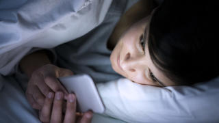 Woman using her phone under blanket in bed at night.